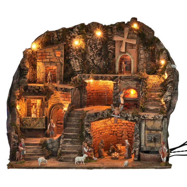 Illuminated nativity scene with statues, fountain, fire, and windmill